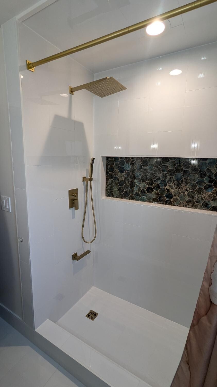 White tiled shower with gold fixtures and hex niche
