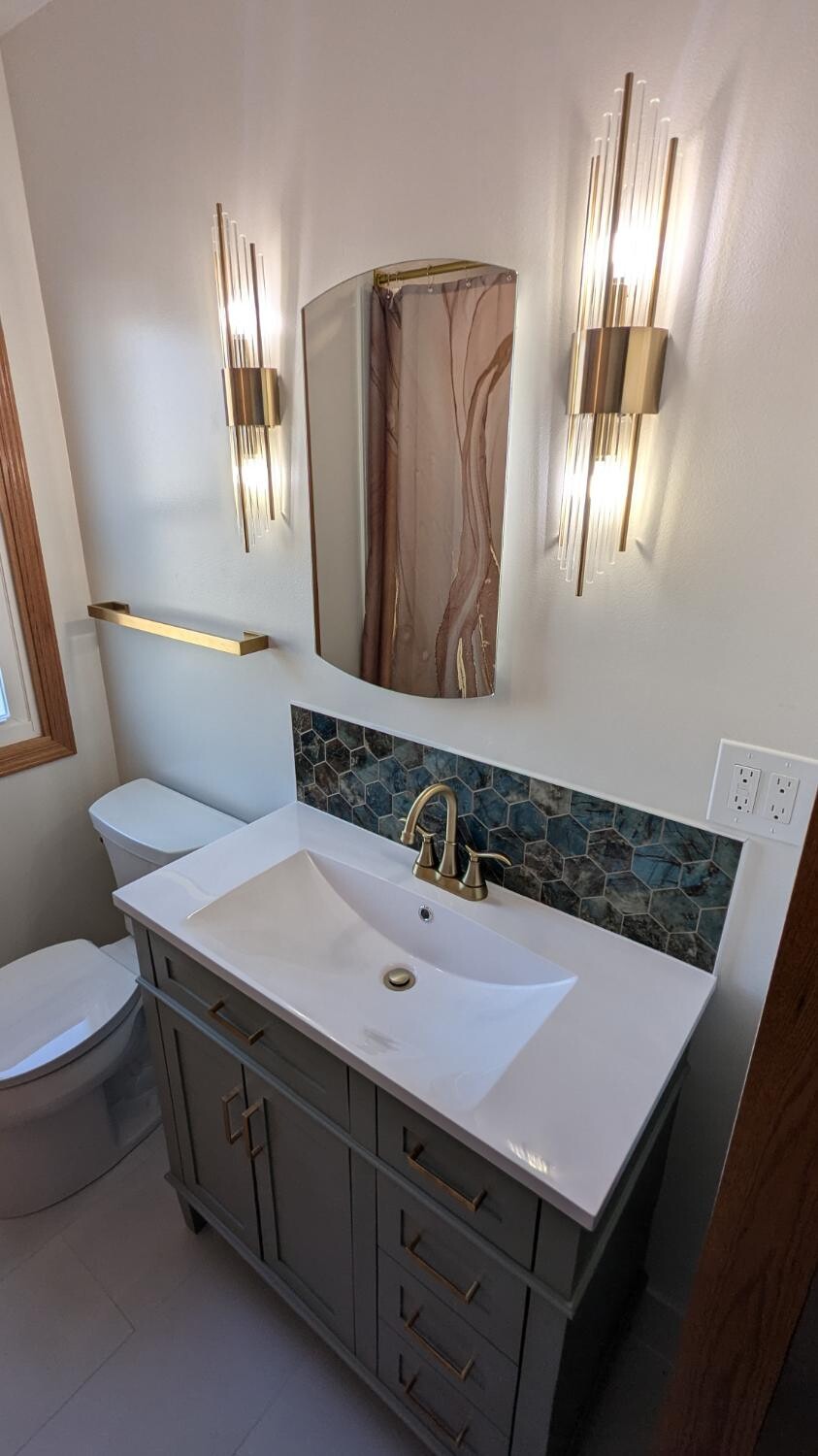 Sage vanity with gold sconces and hex backsplash
