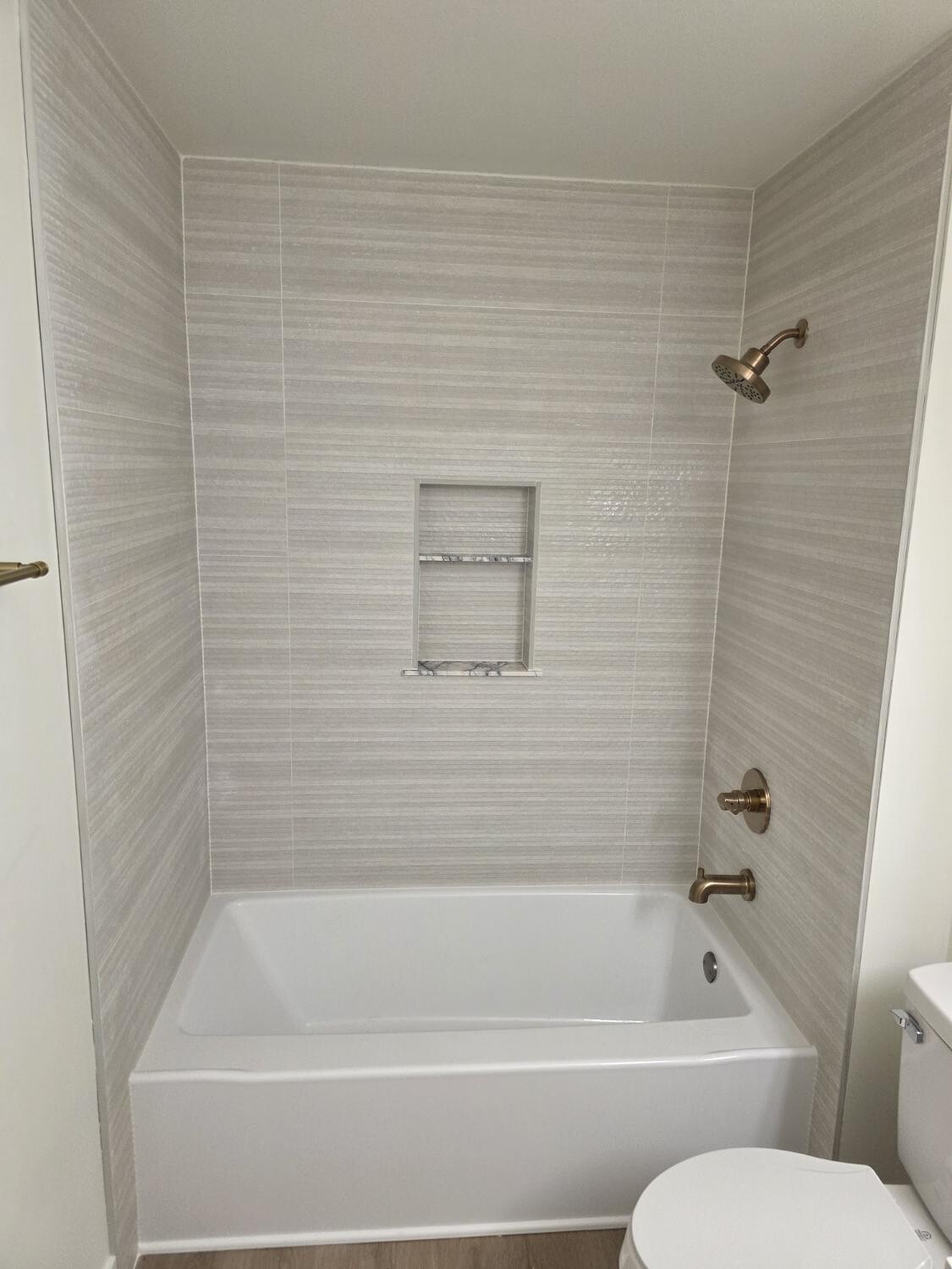 Linear beige tile tub surround with gold fixtures